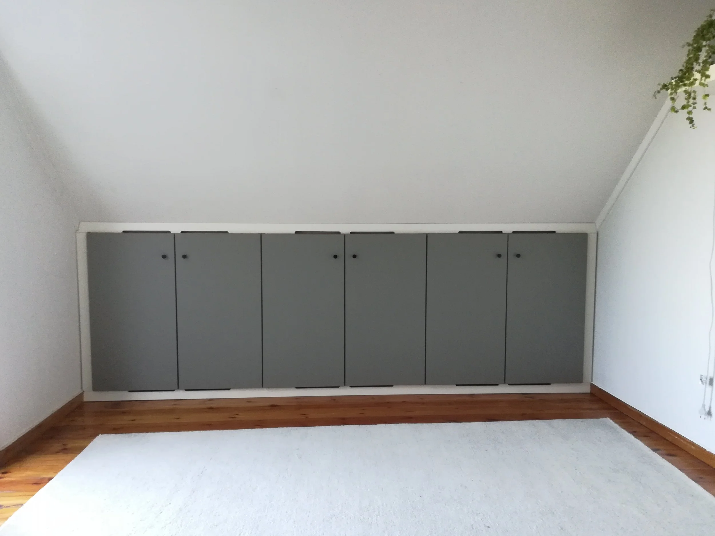 Maßgefertigter Einbauschrank mit grauen Fronten für eine Dachschräge, raumhoch über die gesamte Wandbreite mit passleisten zu allen vier anliegenden Wänden