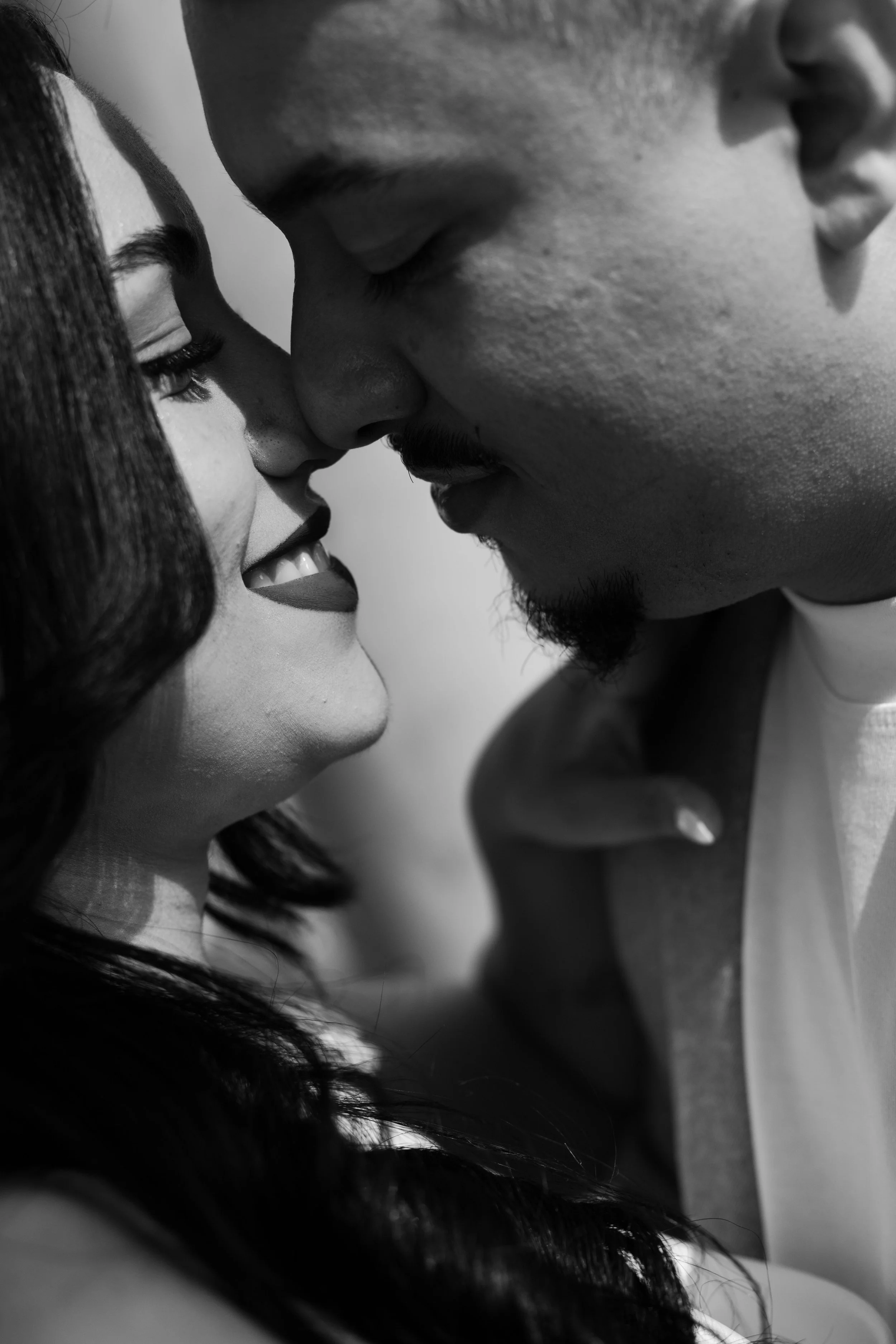 Close-up black and white photo of a couple with foreheads and noses touching, close and intimate moment.