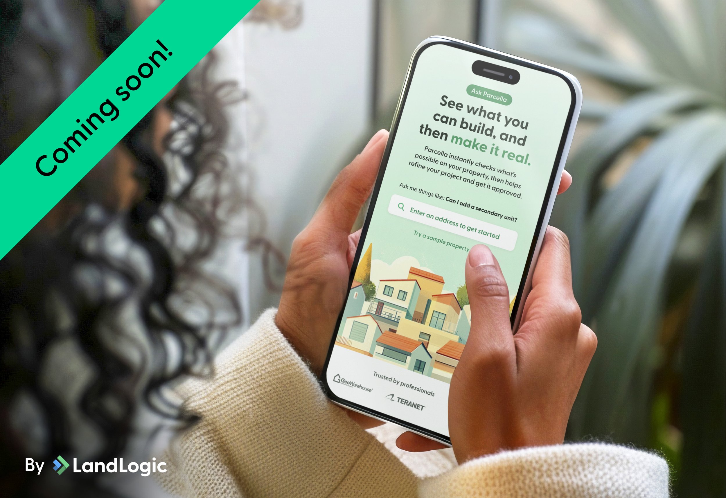 A person holding a smartphone displaying a property app called LandLogic with an illustration of houses and text about building and making real estate projects. The phone is being held in front of green plants and a window. A large green banner on the upper left says 'Coming Soon!'