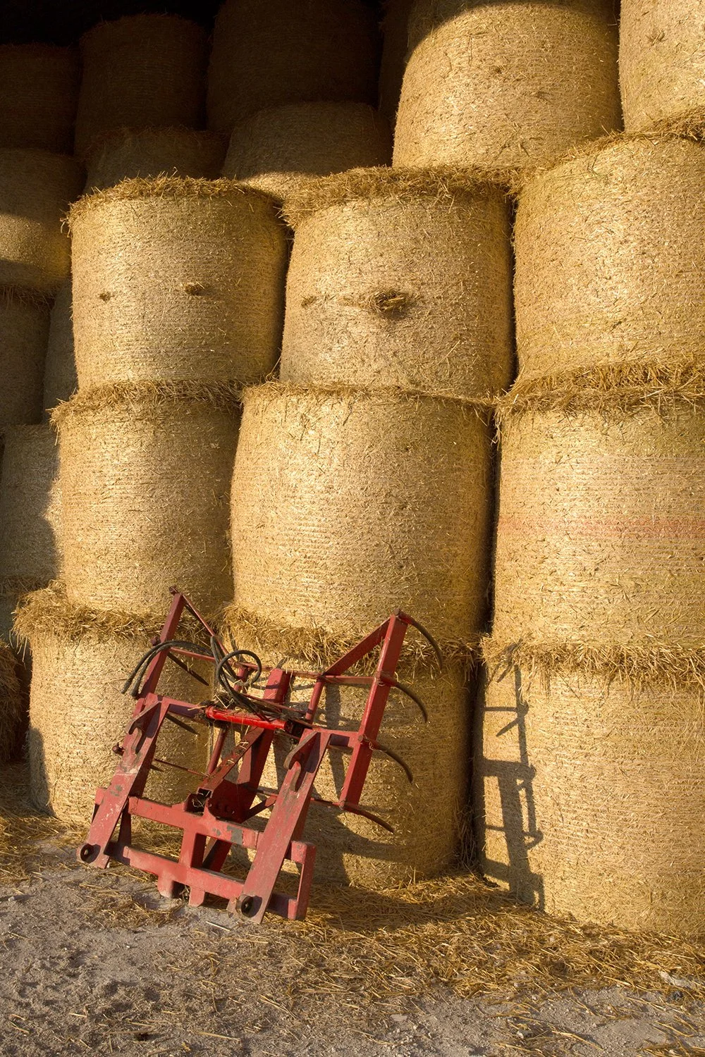 Stacked round hay bales with red farm equipment in front
