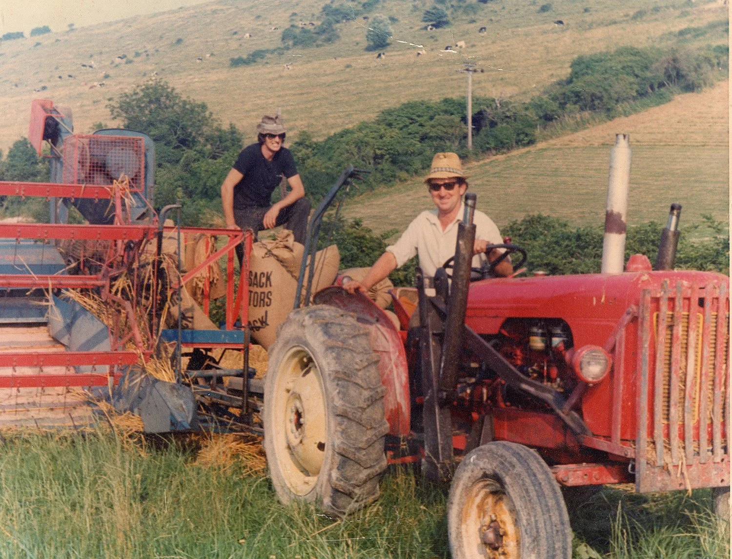 Retro photograph of two men working on a farm with a red tractor and agricultural machinery in a field.