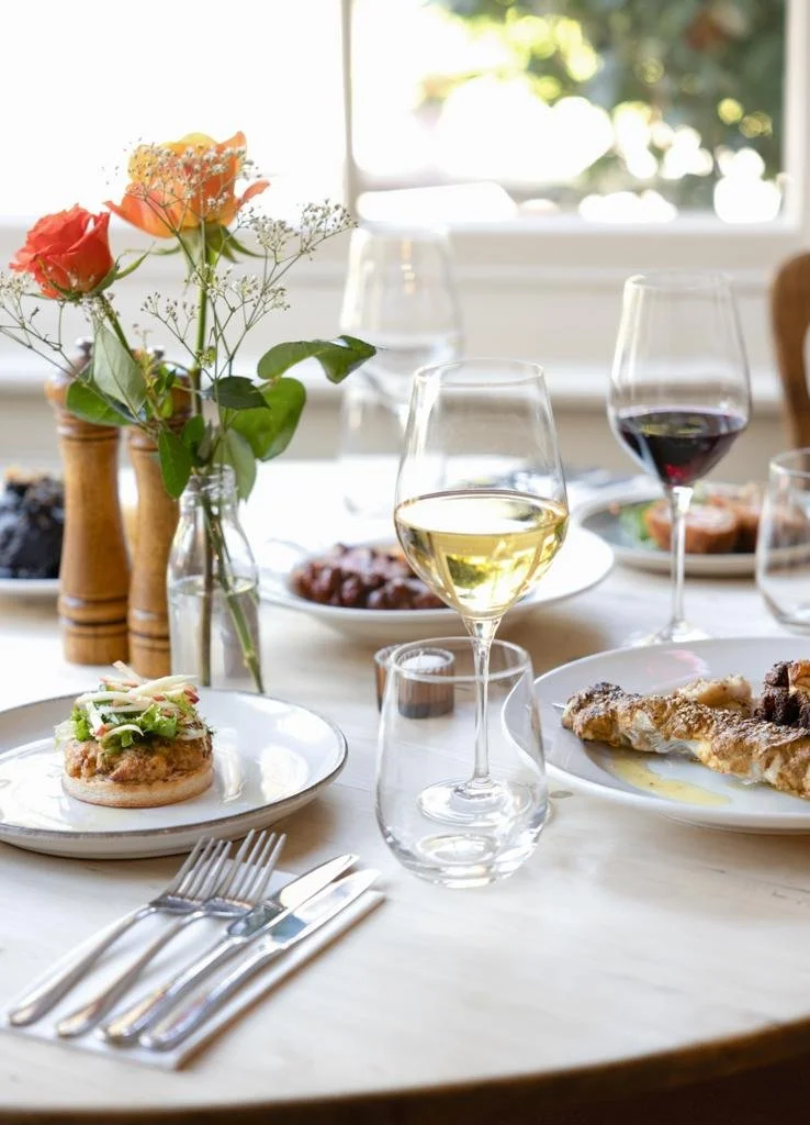 Elegantly set dining table with plates of gourmet food, glasses of white and red wine, fresh flowers in a vase, and cutlery.
