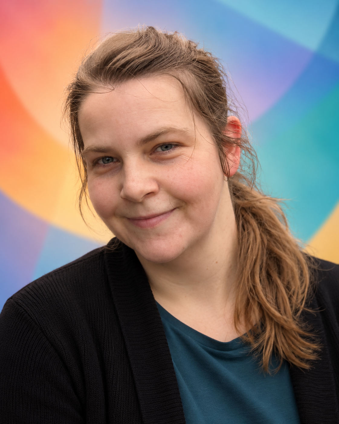 A woman with light brown hair and blue eyes, smiling at the camera, wearing a black cardigan and a teal shirt, with a colorful abstract background.
