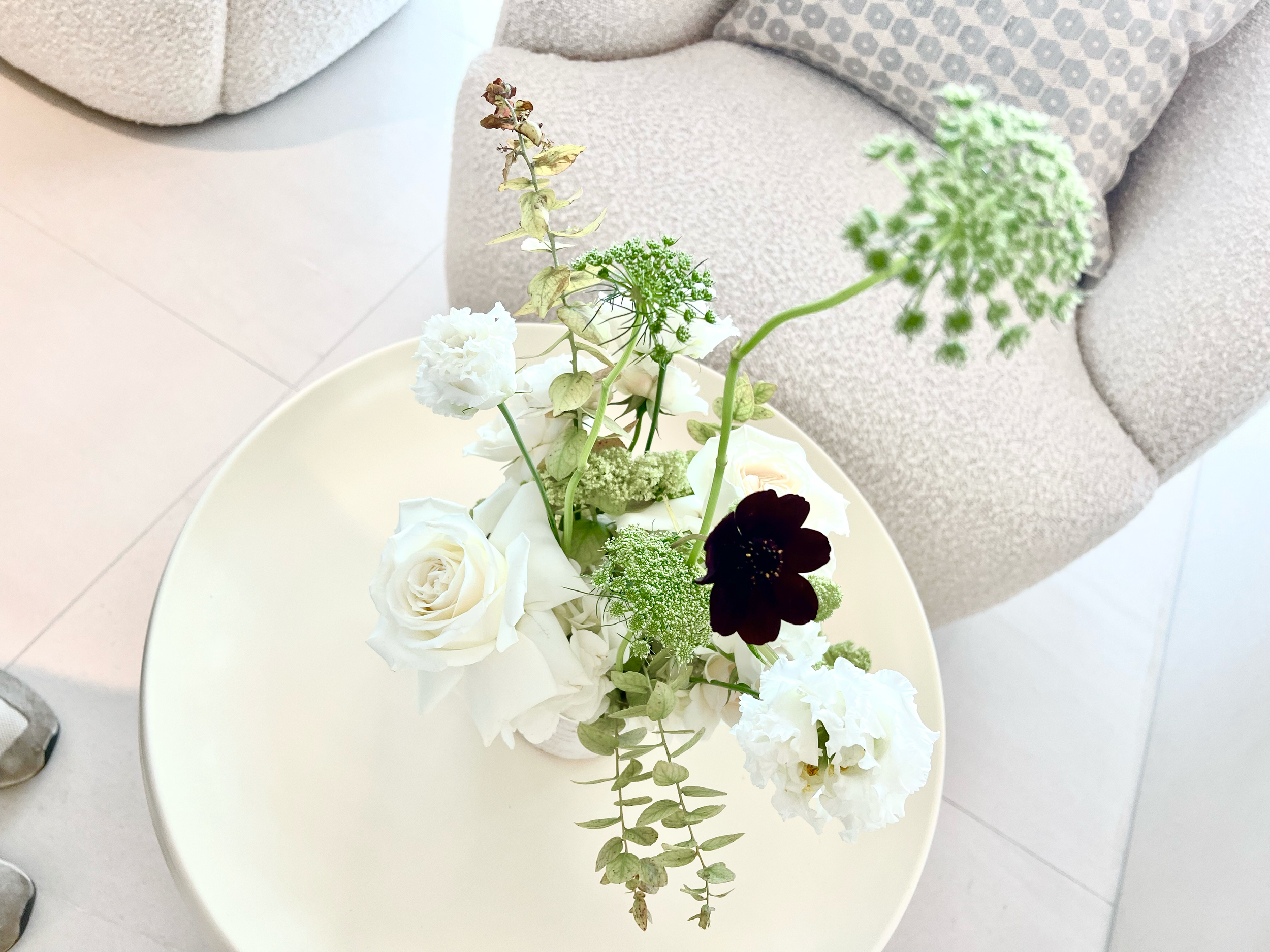 A vase with a mixed arrangement of white and dark flowers and green foliage on a white table.