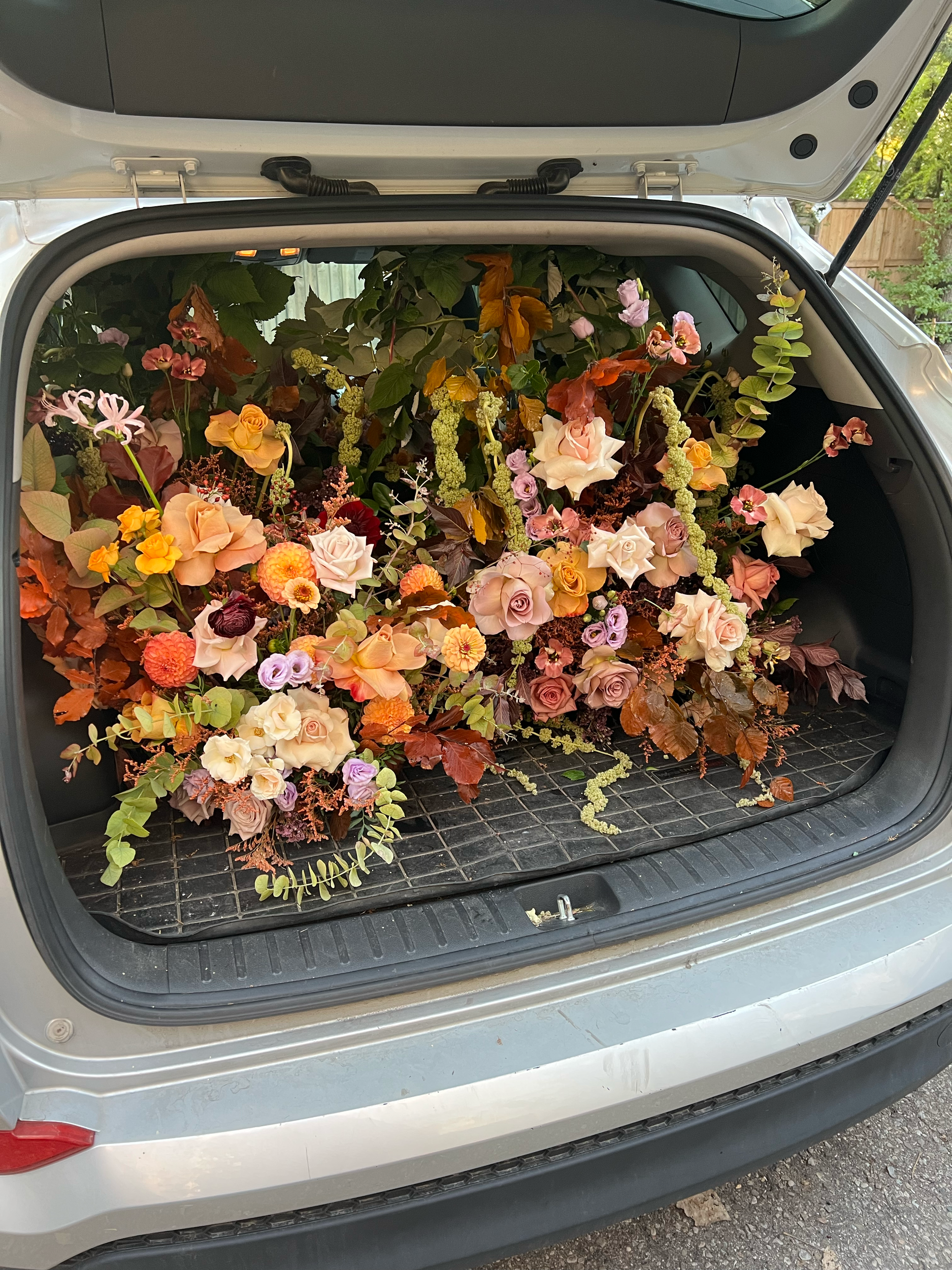 The trunk of a car filled with a large arrangement of various colorful flowers and leaves.