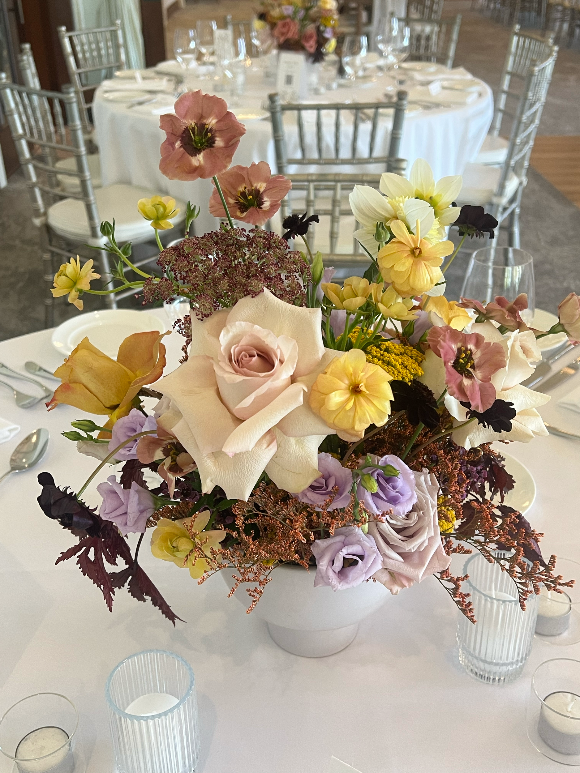 A floral centerpiece with pink, yellow, purple, and white flowers on a decorated banquet table, surrounded by candles and tableware.
