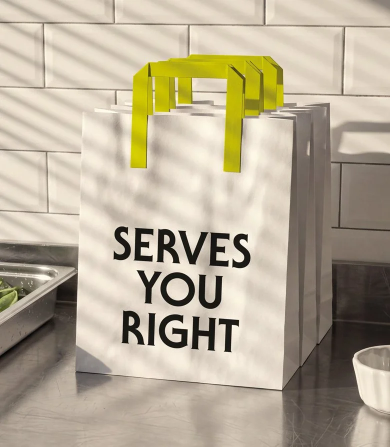 a white paper bag with fluorescent yellow handles and the words SERVES YOU RIGHT in large black letters