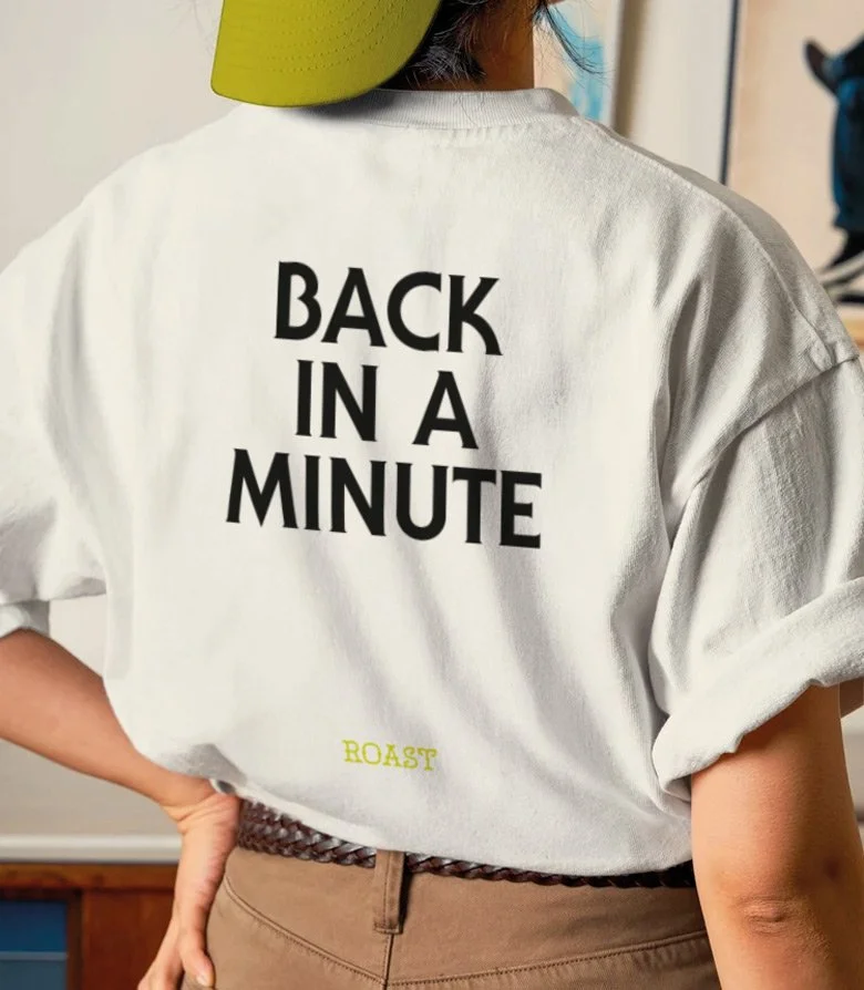a women in a white t-shirt with 'back in a minute' in large black letters above a fluorescent yellow ROAST logo