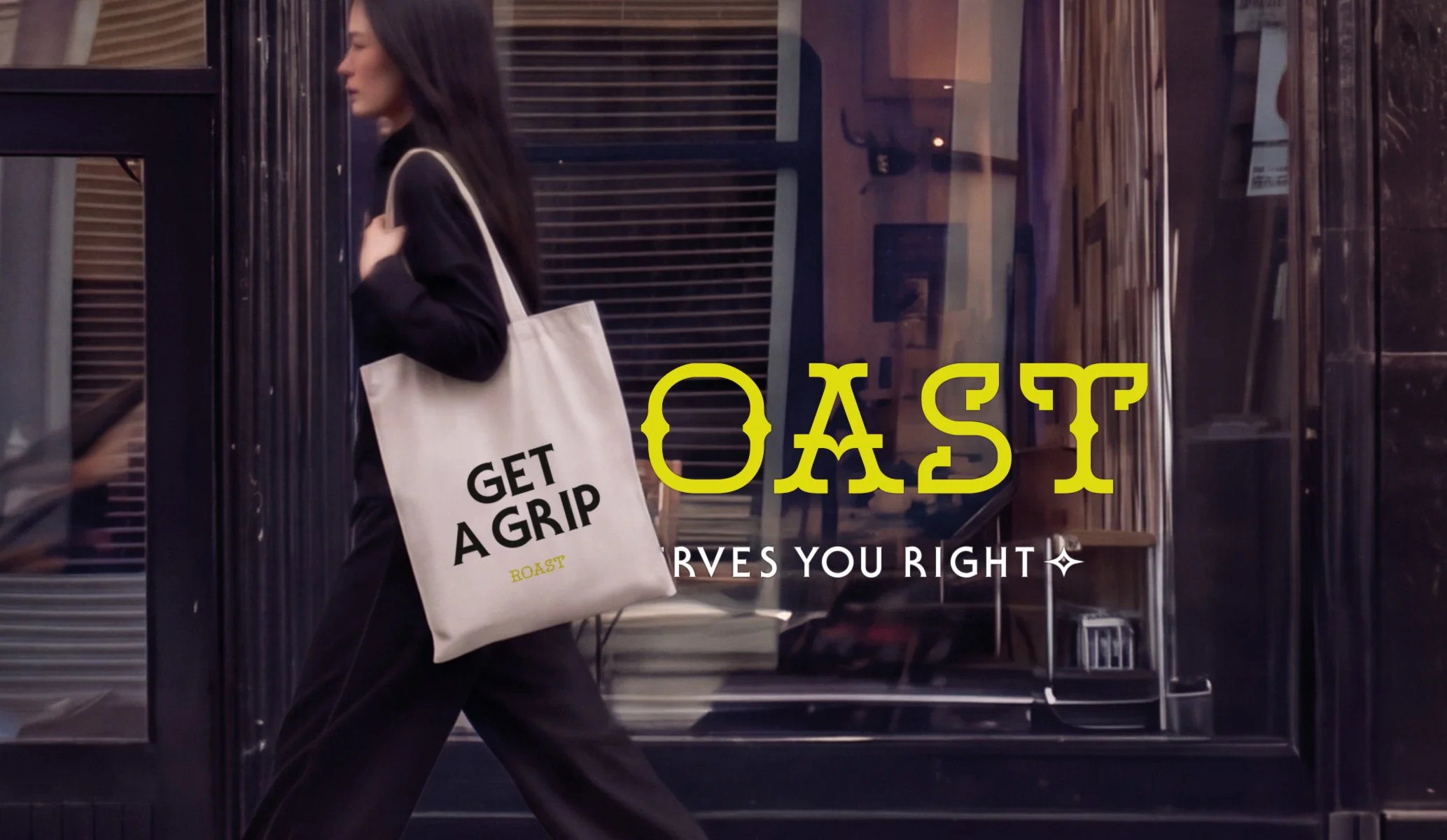 a women walking past a shop window with a tote back on here shoulder showing the words 'get a grip' above a fluorescent yellow logo for ROAST