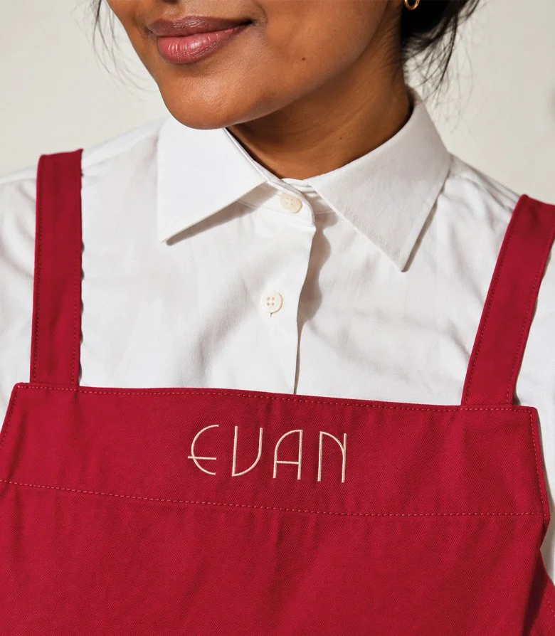 A Asian women in a white shirt and magenta apron with an embroided Evan Bakery logo