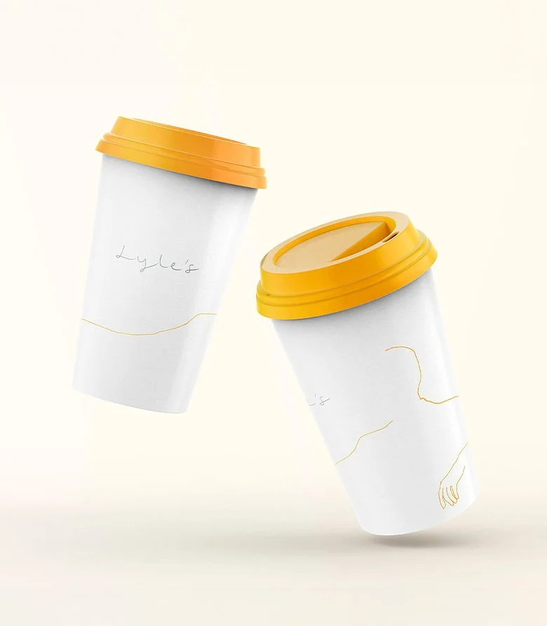 white takeaway coffee cups with yellow lids featuring the Lyle's logo for the restaurant at Lyle Hotel in Washington DC created by Colt