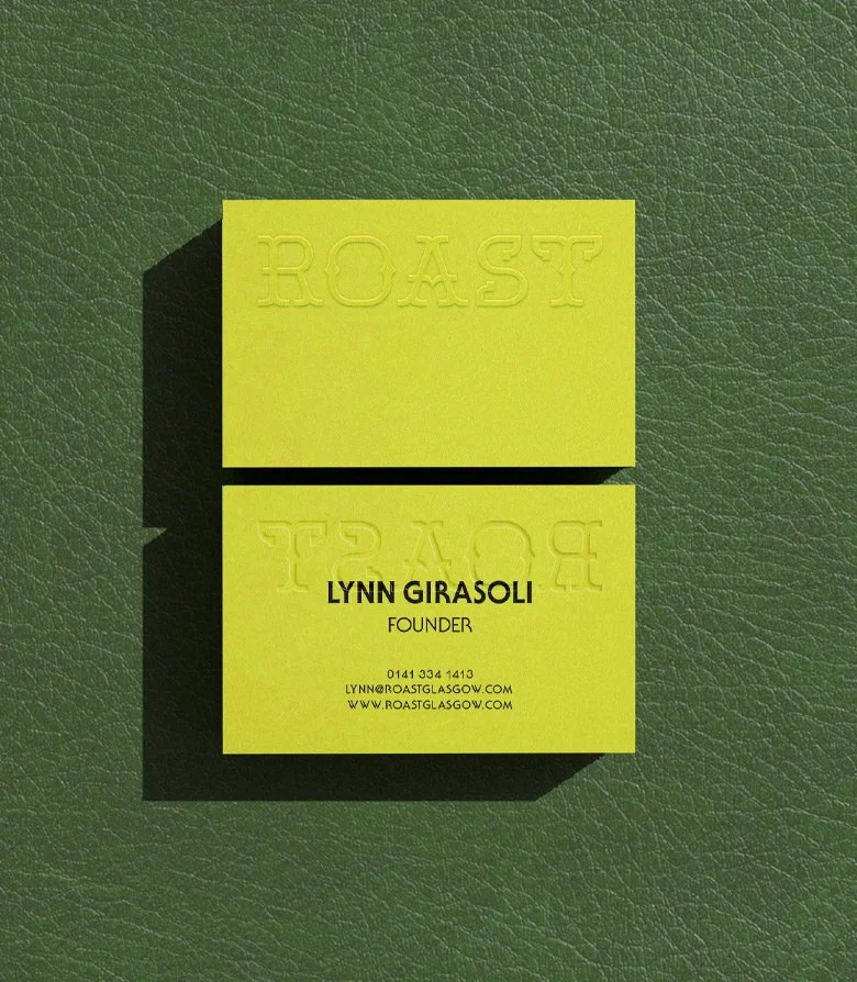 fluorescent yellow business card with a blind embossed ROAST logo on one side and contact details on the other against a green leather surface