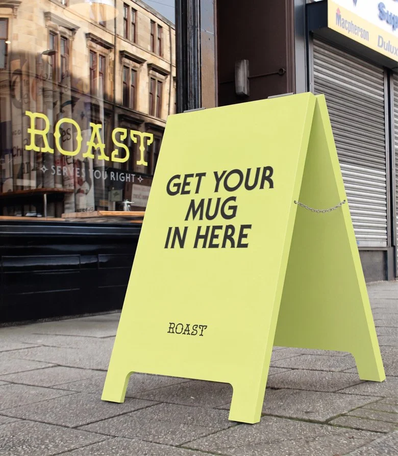 fluorescent yellow sandwich board on a Glasgow street showing the words 'Get your mug in here' above the ROAST logo