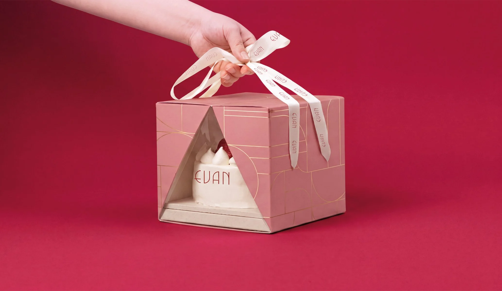 A hand holding the ribbon of a pink, branded cake box for Evan Bakery in Al Ain