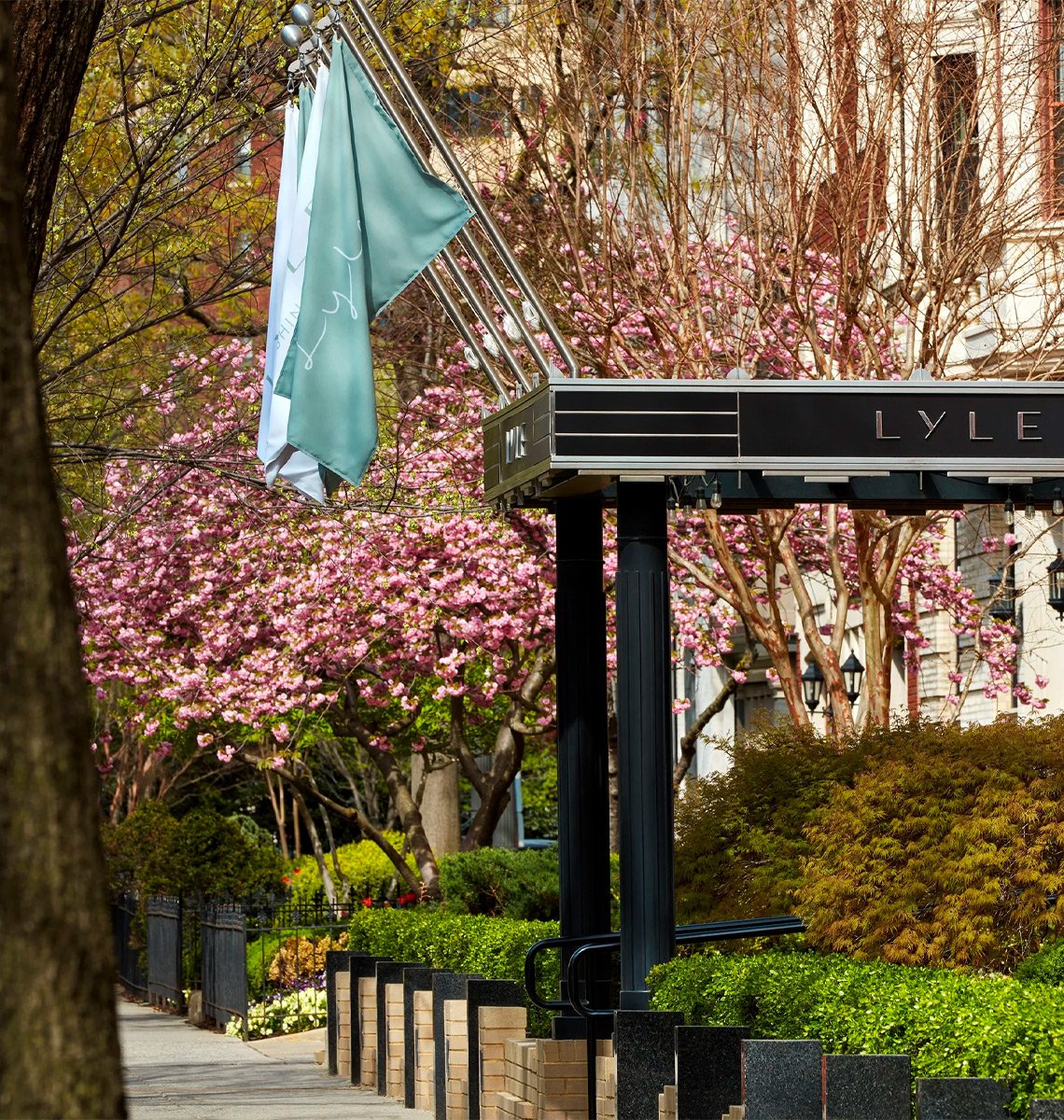 Entrance to Lyle Hotel in Washington DC surrounded by spring blossom trees showcasing hotel branding.