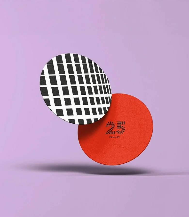 two coasters, one featuring a black and white pattern and the other in red and the logo for 25 Paul St by Colt