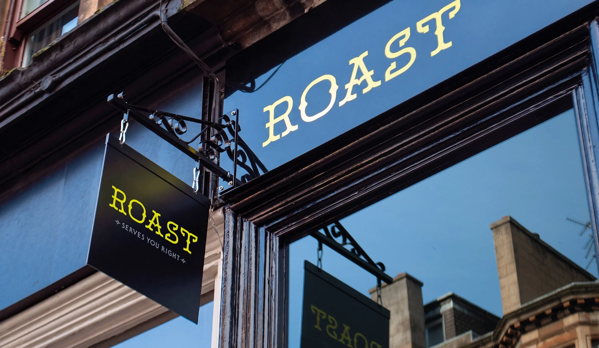 hanging black blade sign with ornate metal work showing a fluorescent yellow ROAST logo
