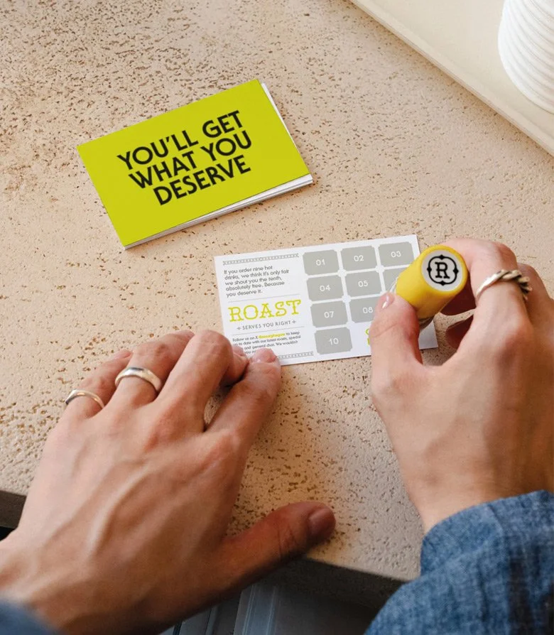 a coffee loyalty card being stamped below a fluorescent yellow side that reads 'you'll get what you deserve'