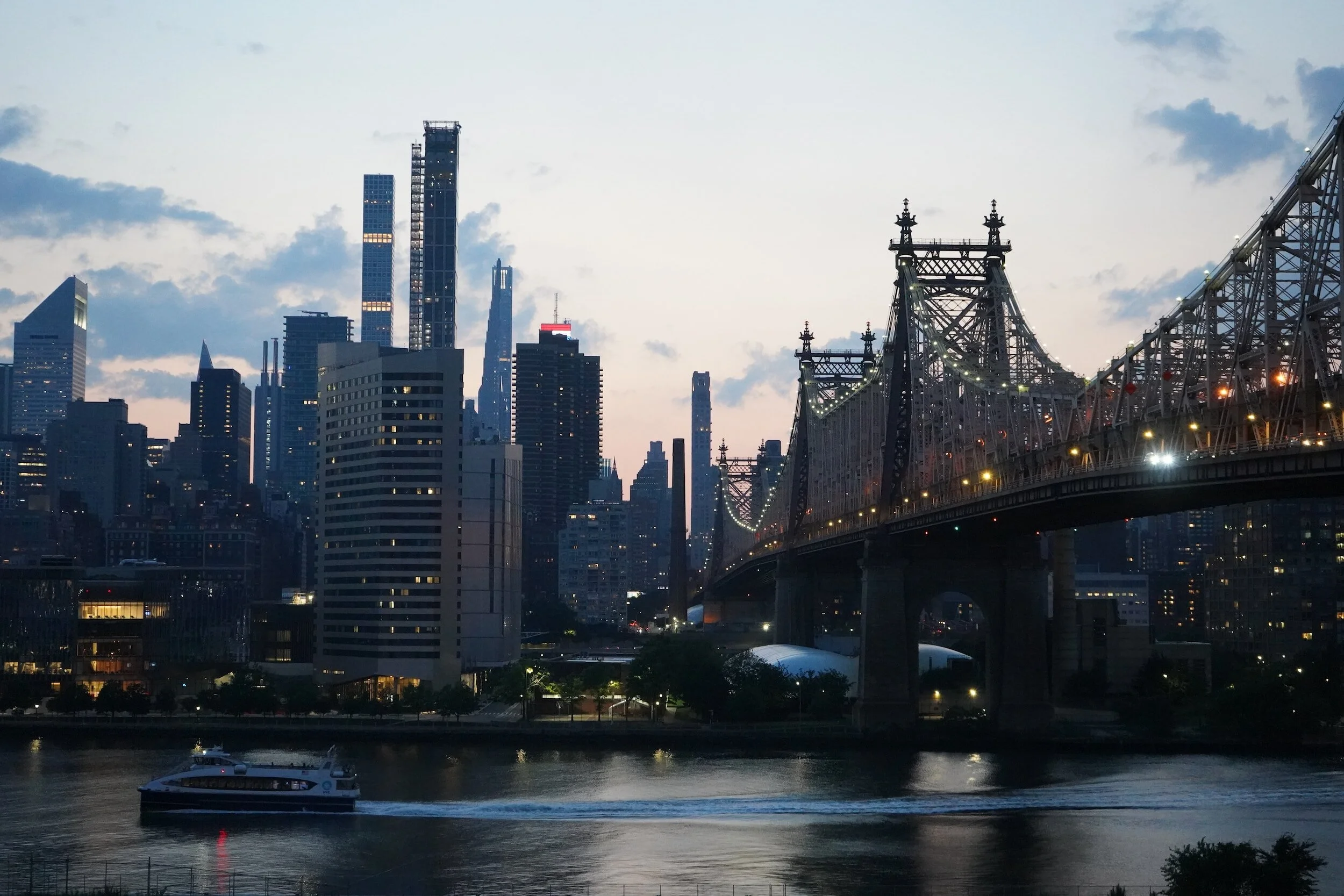 A city skyline with a bridge in the foreground. The bridge is the Ed Koch Queensboro Bridge, which is located in New York City. The city skyline includes the Empire State Building and other iconic buildings.