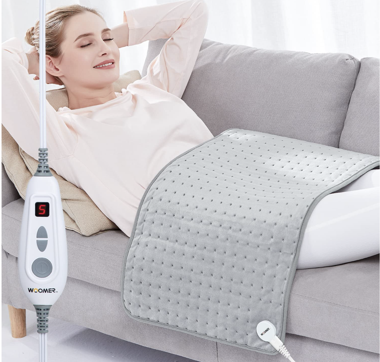 Woman laying on a couch with arms behind her head using a large gray heating pad across her abdomen