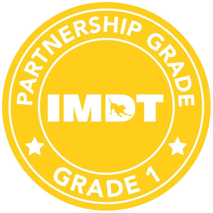A yellow circular badge with white text that reads 'Partnership Grade 1' and 'IMD'T' in the center, with a small dog silhouette inside the letter 'D'.