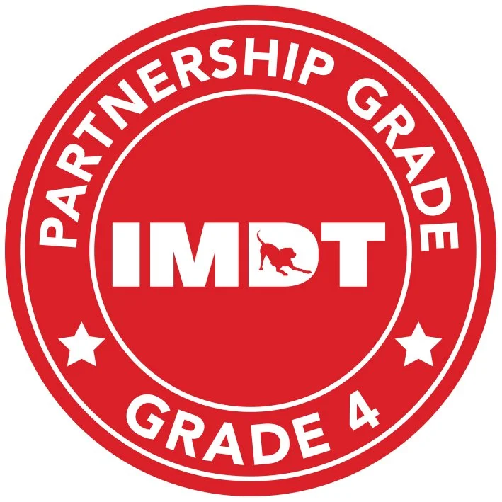 Red circular badge with white text and stars, reading "Partnership Grade 4" and featuring the IMDT logo with a stylized dog.