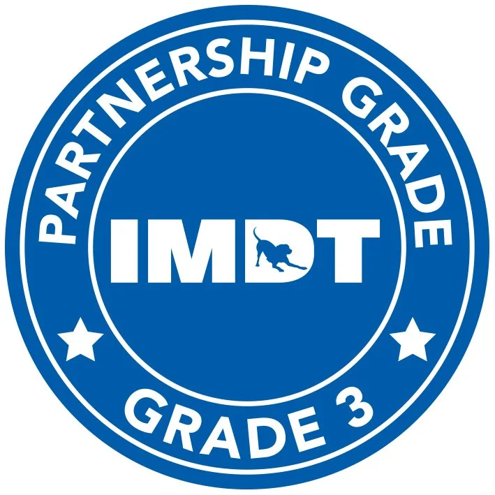 A blue circular badge with white text that says 'Partnership Grade 3.' In the center, there is a logo with the word 'IMPACT' and a silhouette of a dog inside the 'D.'