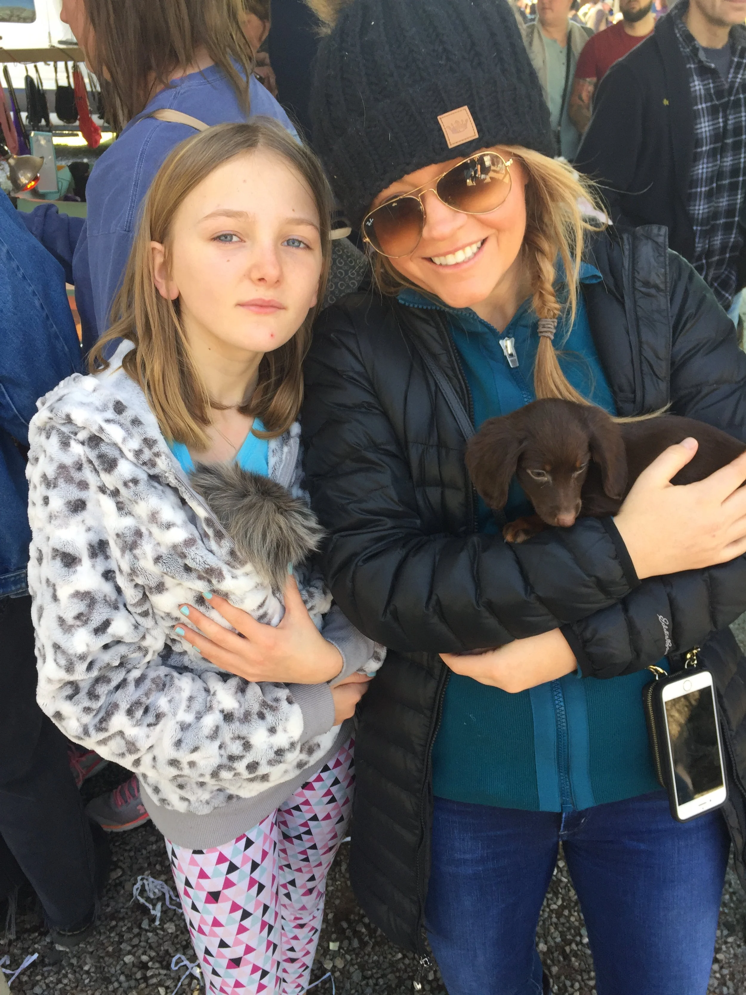 Two women holding small dogs in an outdoor crowded setting.