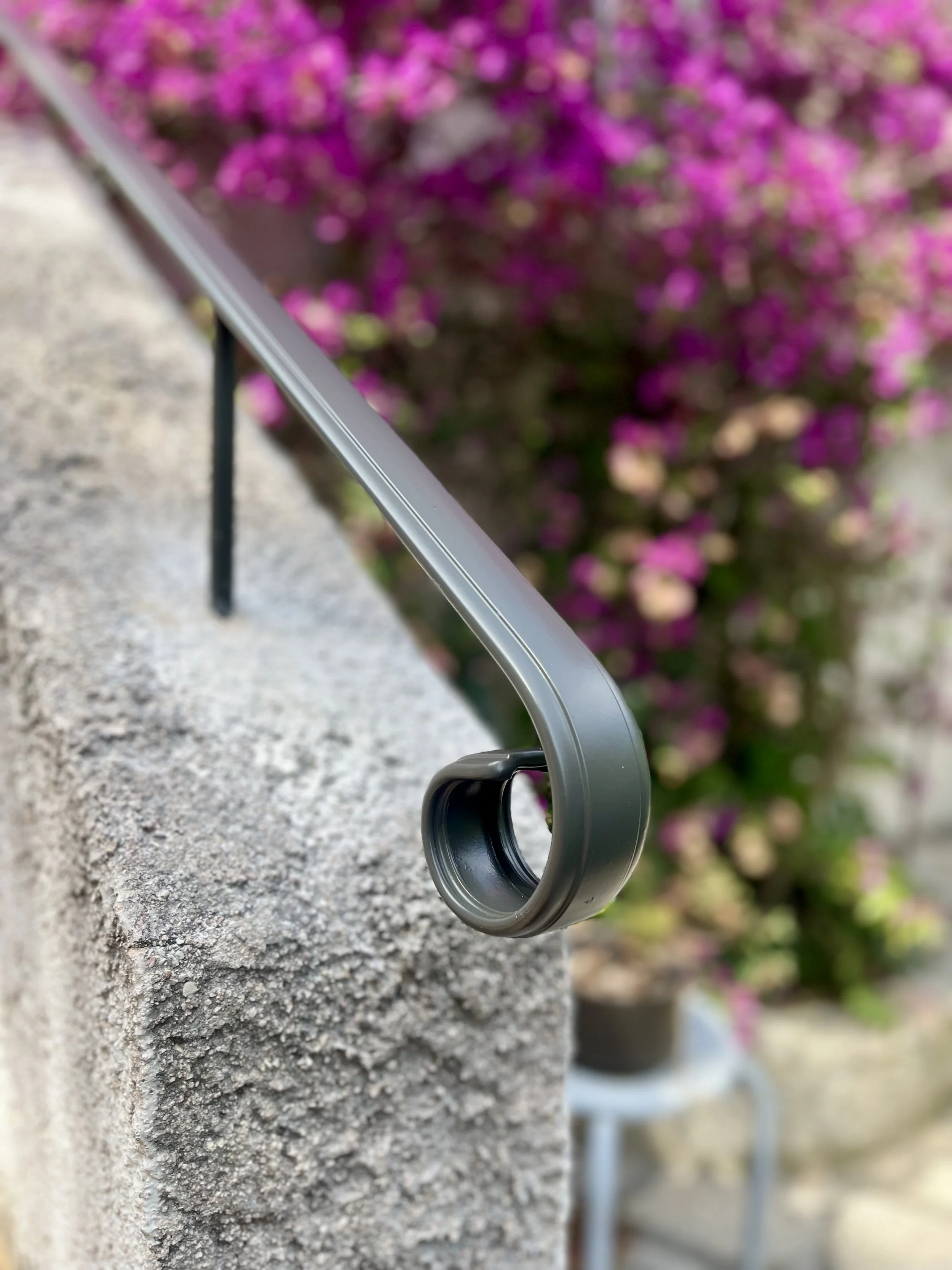 Prise de vue en angle d'une tablette posée sur une tablette en béton, avec un fond de buissons de fleurs roses.