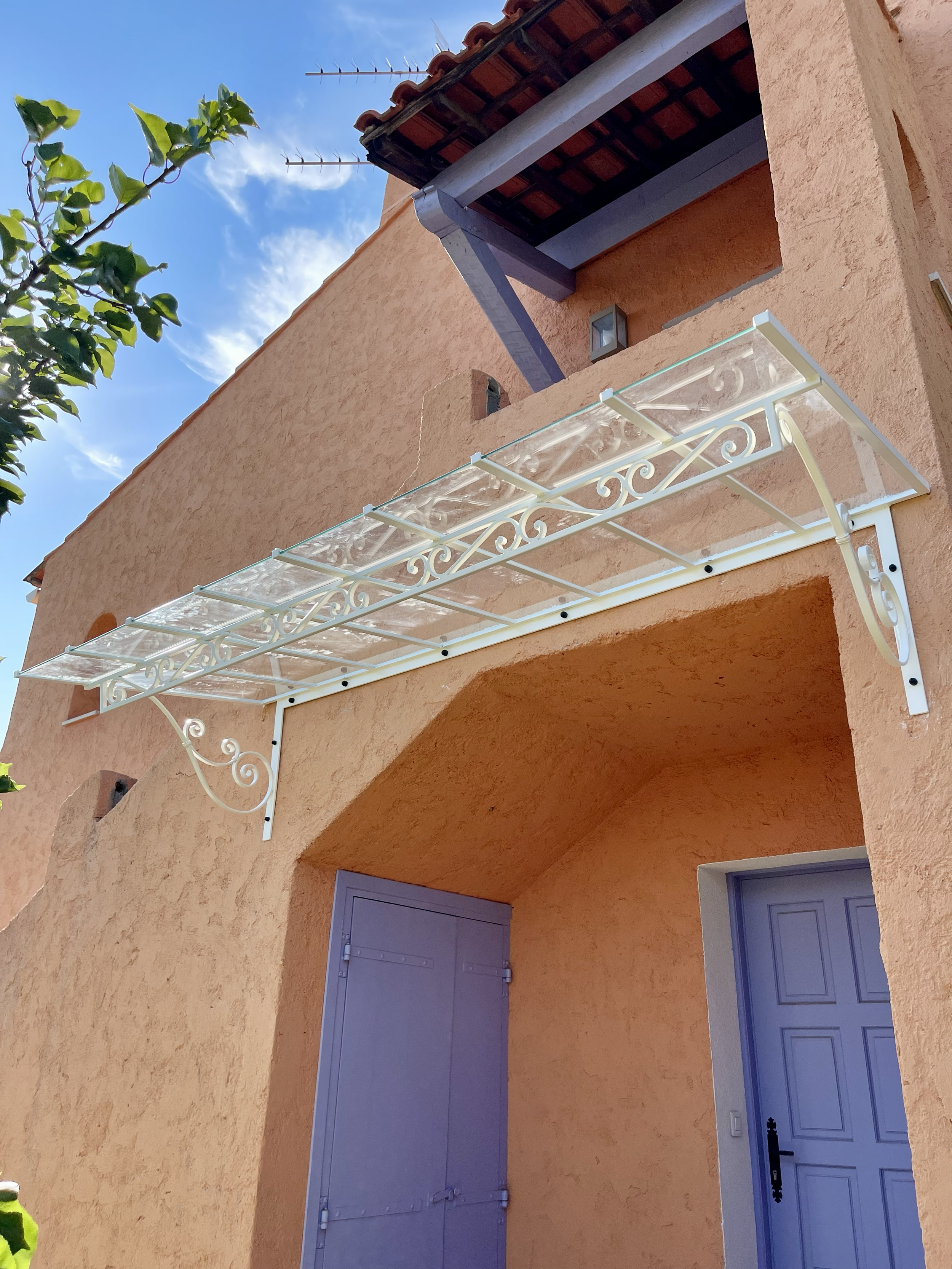 Façade d'une maison en terrasse avec porte gris foncé, volets grisés, et un balcon avec un bardage en verre et structure en fer blanc.