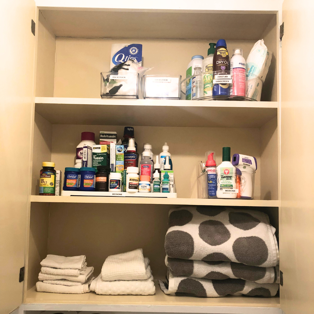 Bathroom cabinet with medicine supplies, towels, and personal care items organized on shelves.