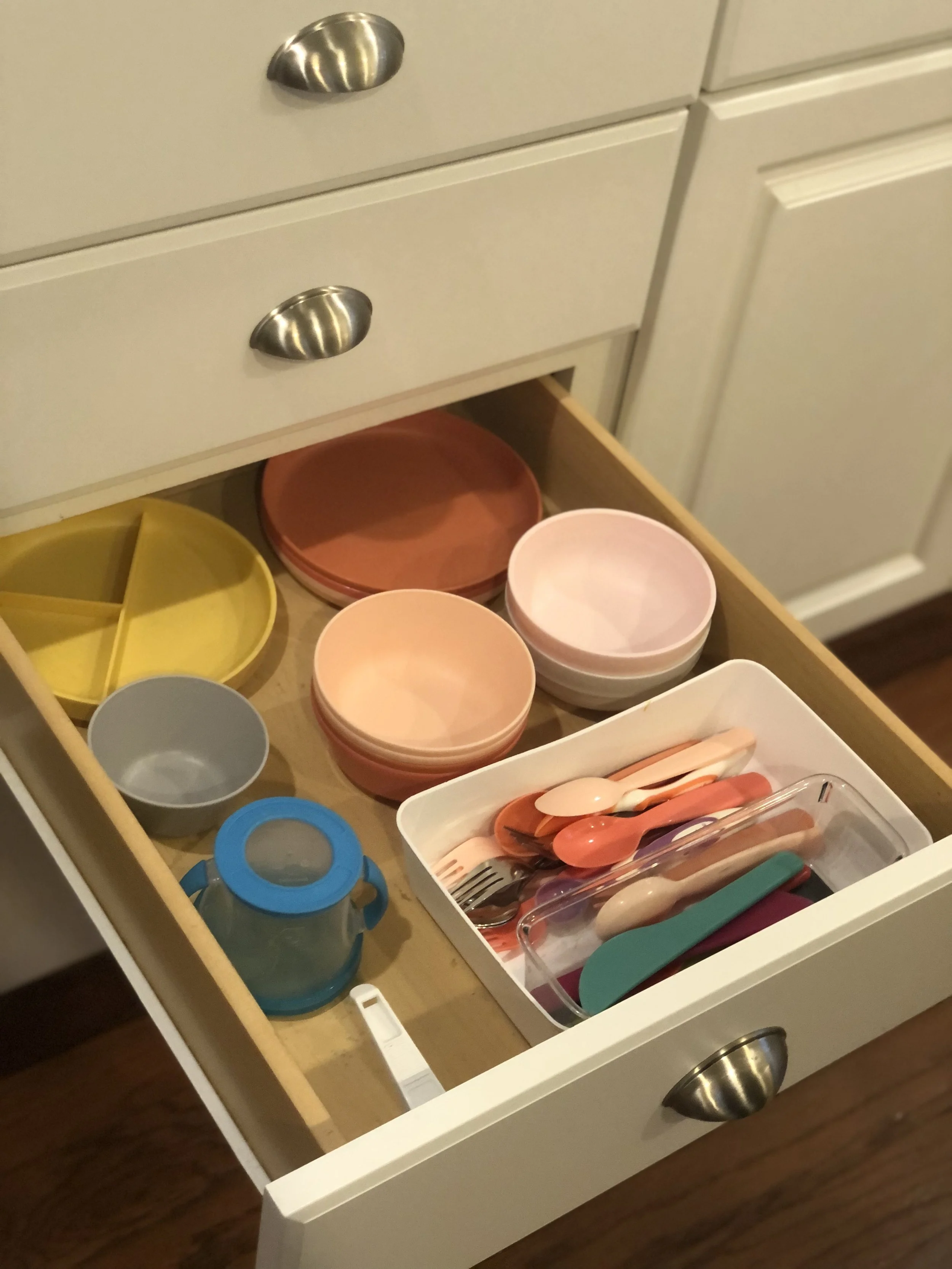Open kitchen drawer containing colorful bowls, utensils, and a small blue bottle.