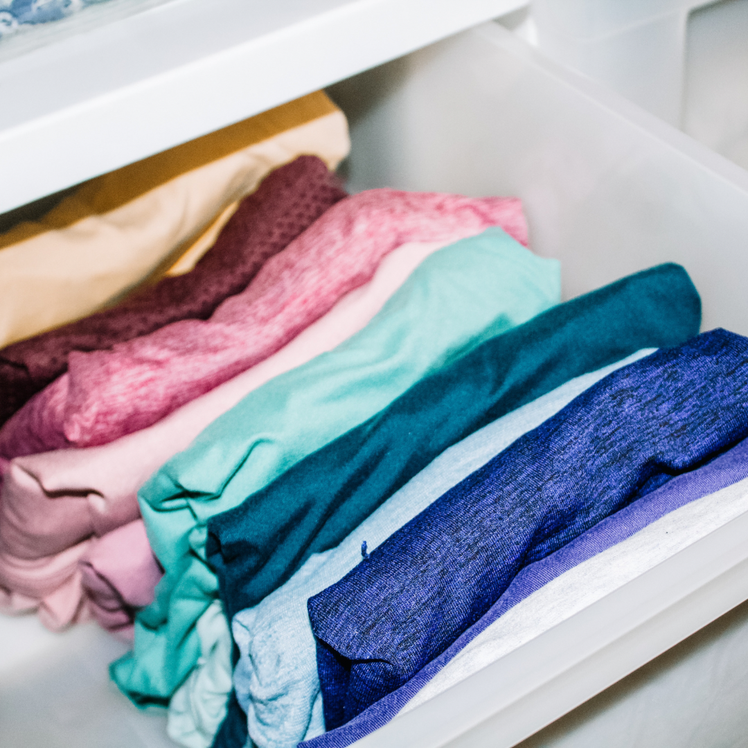 Colorful folded clothes in a white drawer.