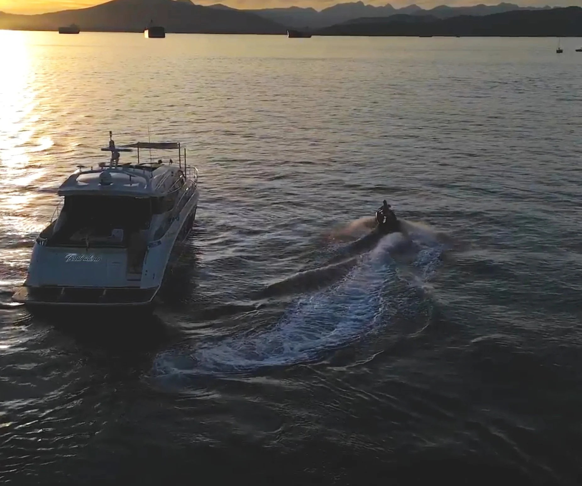 A boat and a jet ski moving on a body of water during sunset with mountains in the background.
