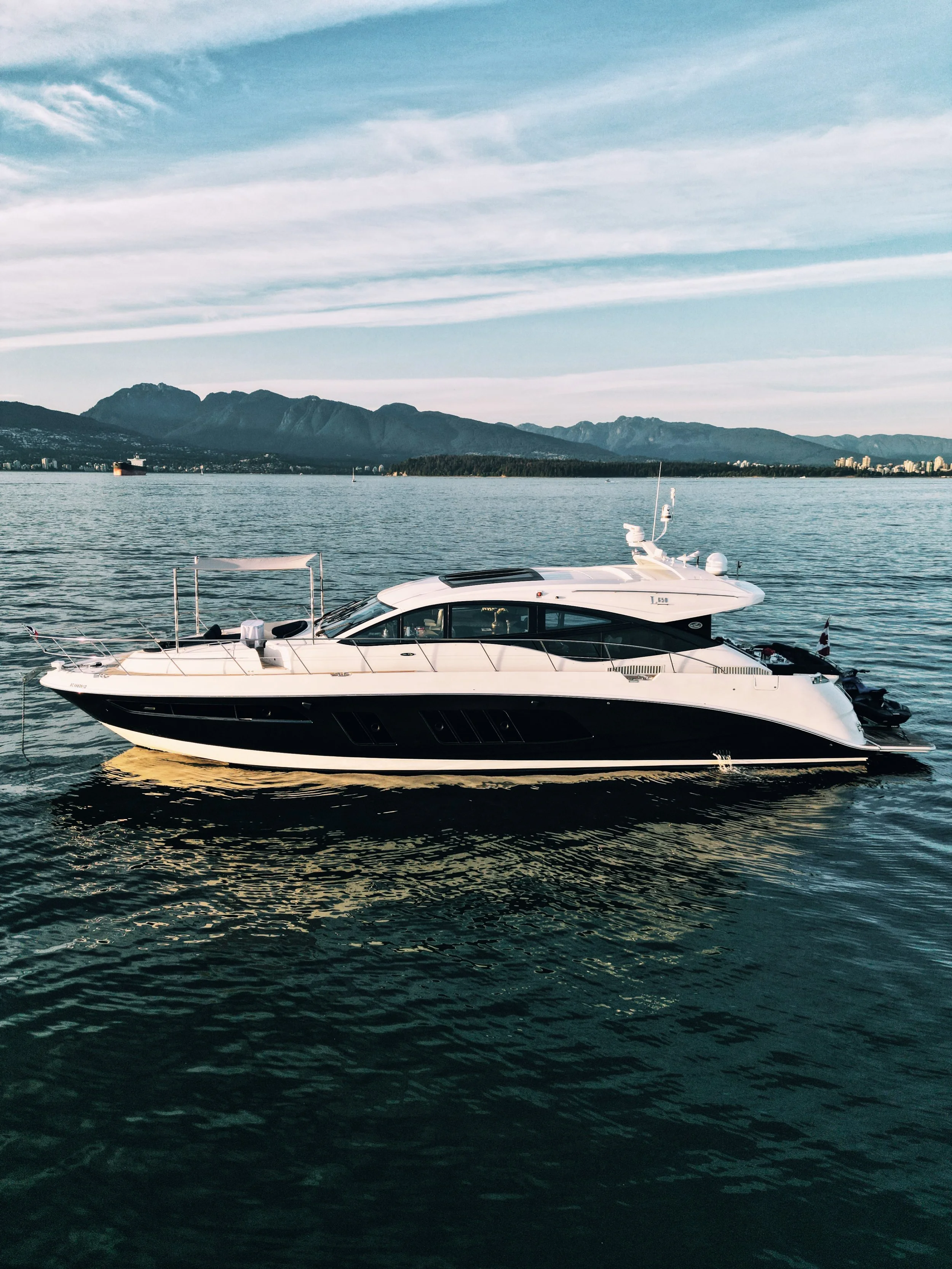 A yacht floating on a calm body of water with a mountain range in the background under a partly cloudy sky.