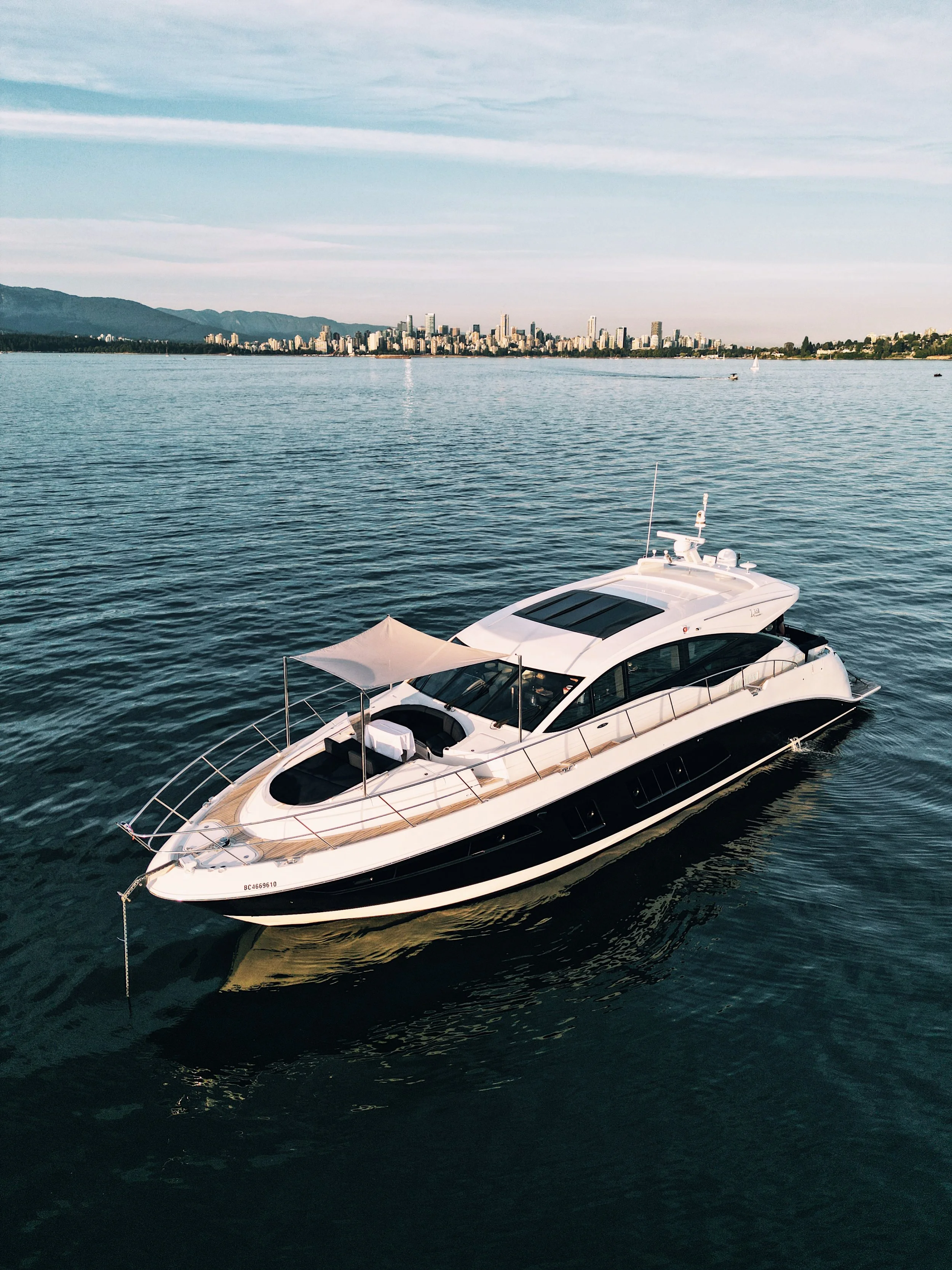 A luxury yacht floating on calm water with a city skyline and mountains in the background.