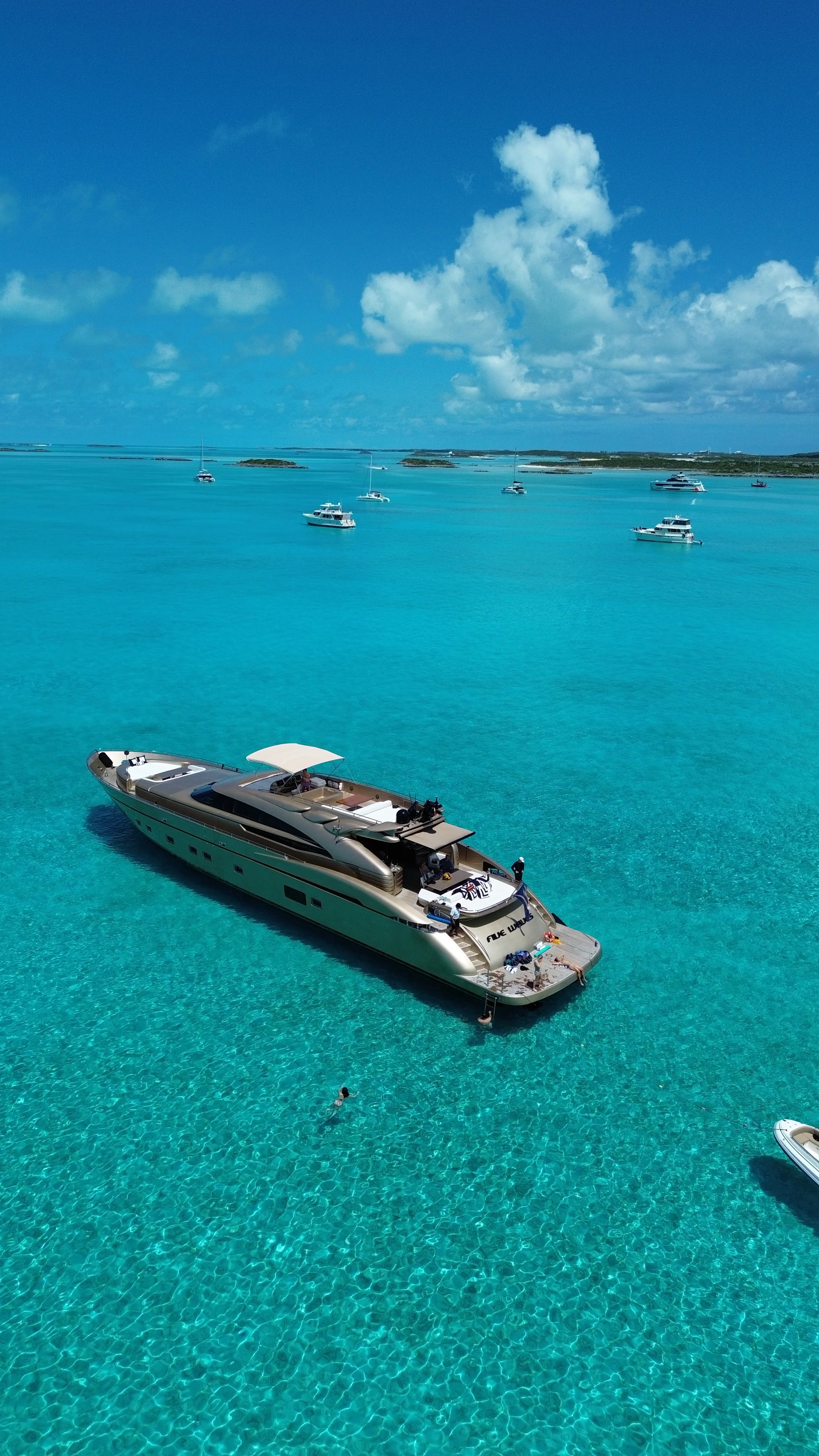 A white luxury yacht cruising at sea, with a jet ski on the back, and islands in the background.