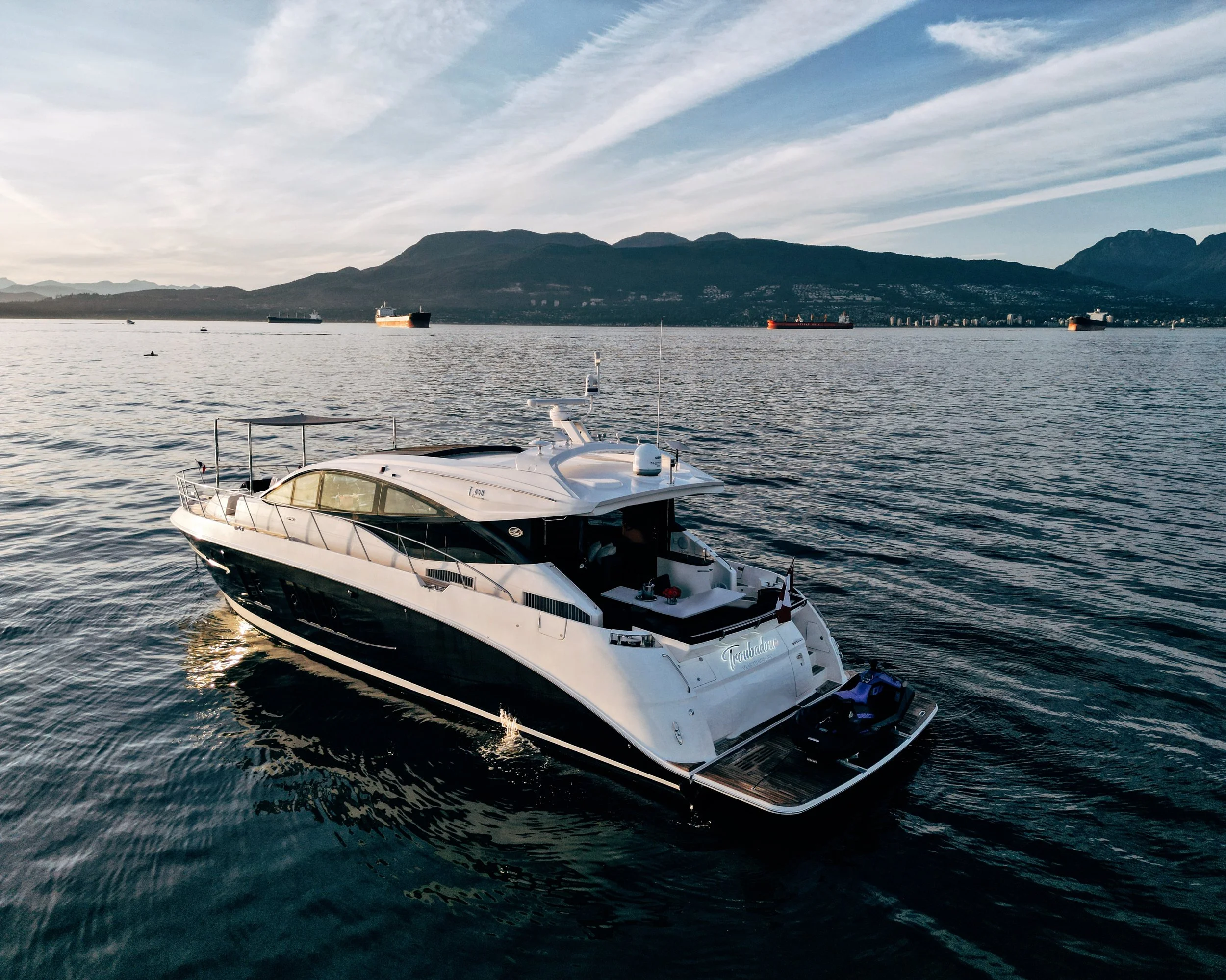 A large white yacht named 'Tranquility' floating on calm water with a backdrop of mountains and a partly cloudy sky.