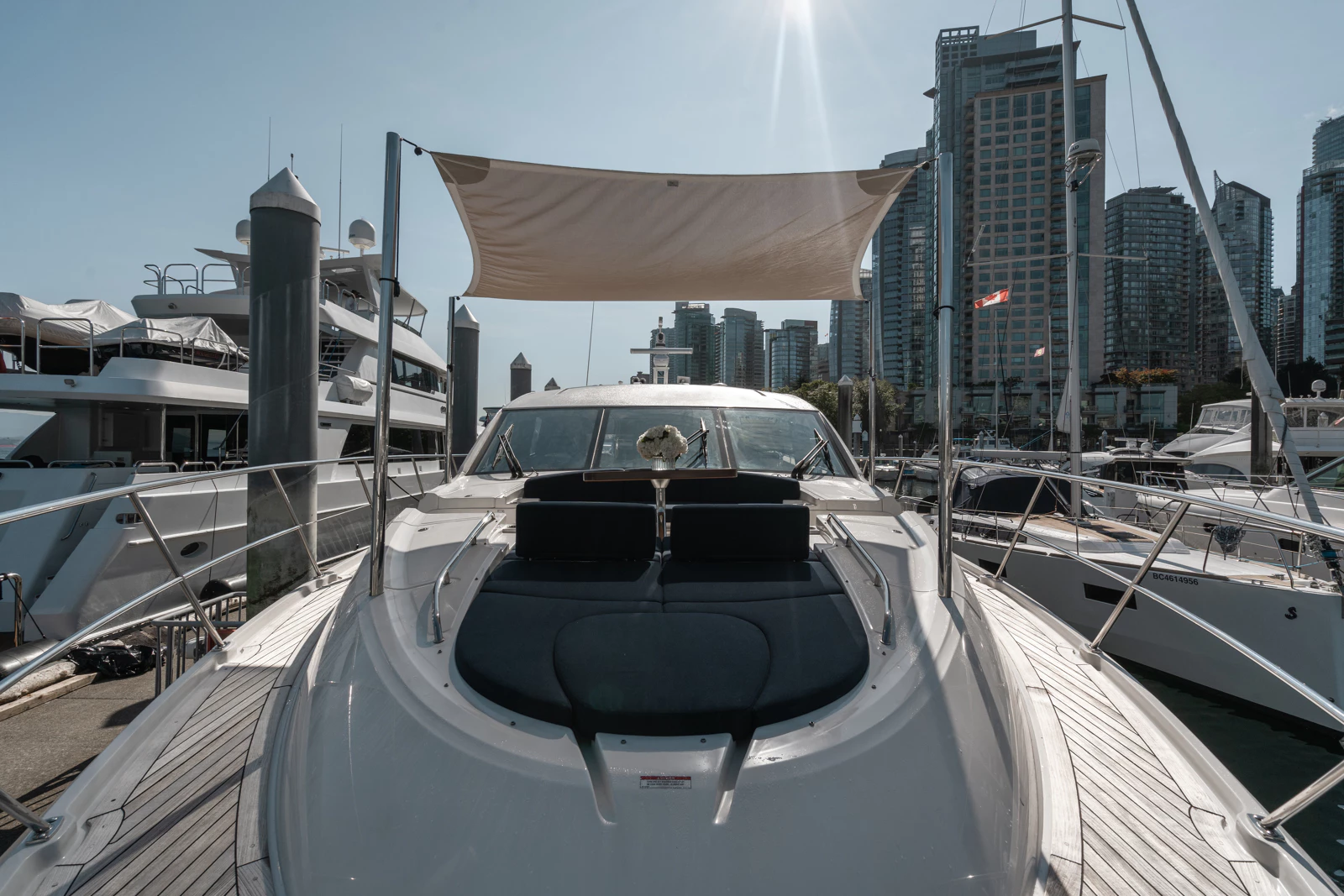 View of a luxury yacht docked at a marina with modern high-rise buildings in the background on a sunny day.