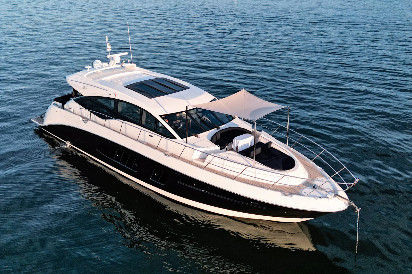 A white and black luxury yacht floating on calm water with a beige sunshade and modern design.