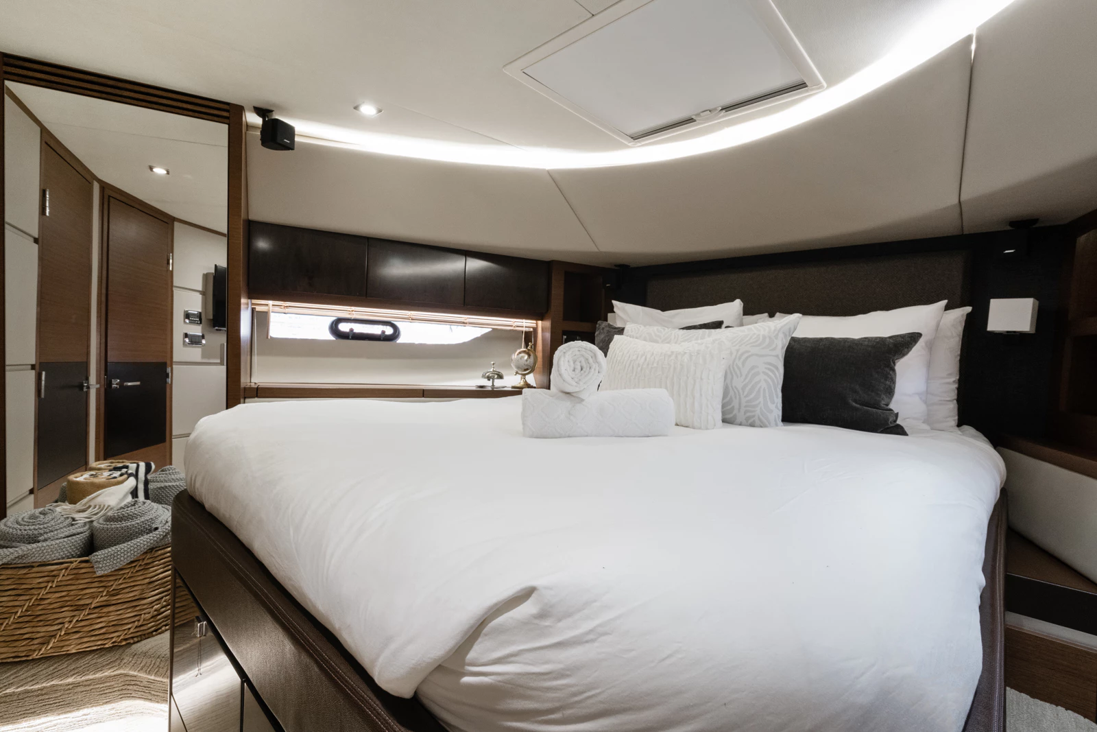Luxurious bedroom with white bedding, decorative pillows, rolled towels, and a window with blinds, in a modern interior
