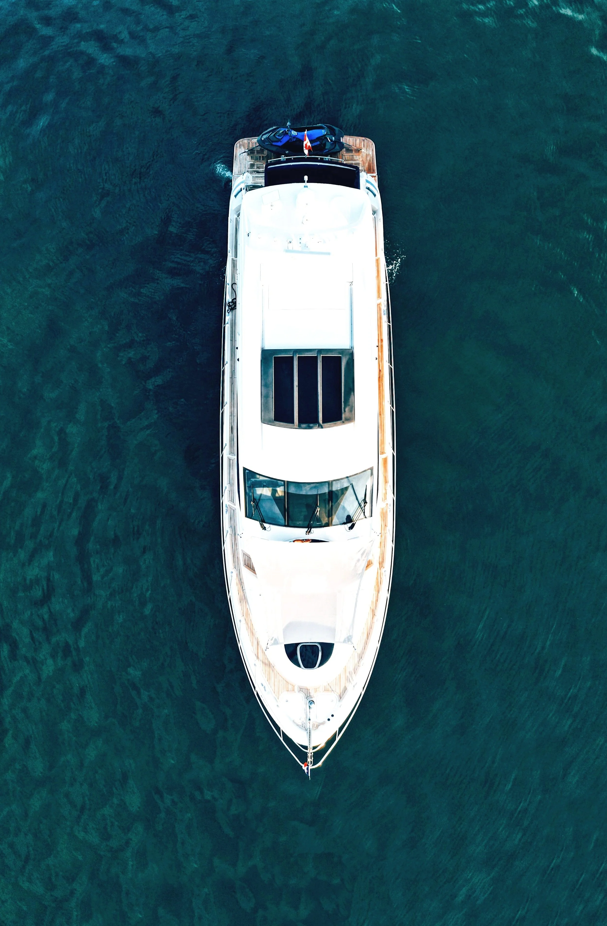 An aerial view of a large white yacht floating on dark green water.