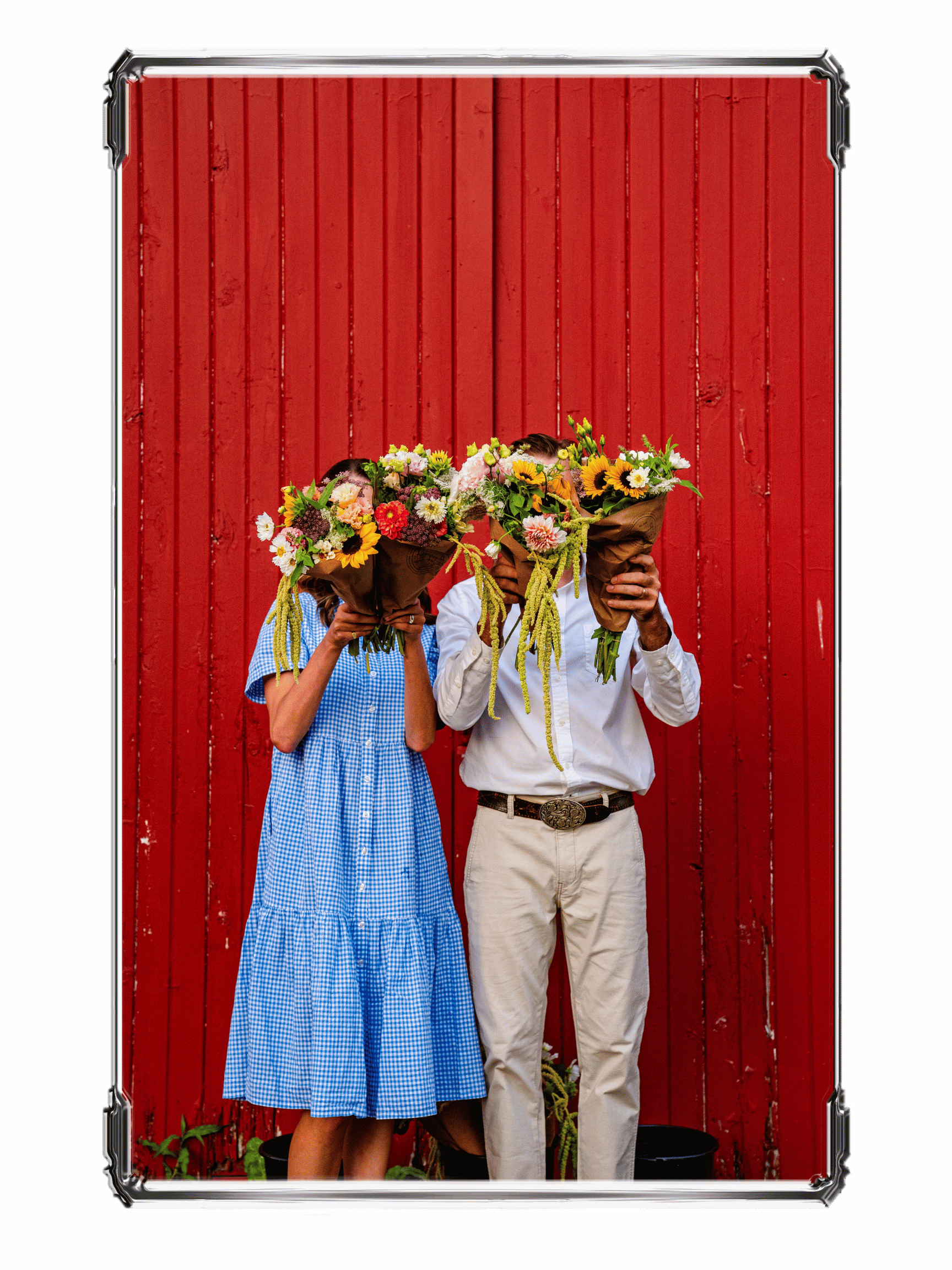 A couple holding large bouquets of colorful flowers in front of a red wooden wall.