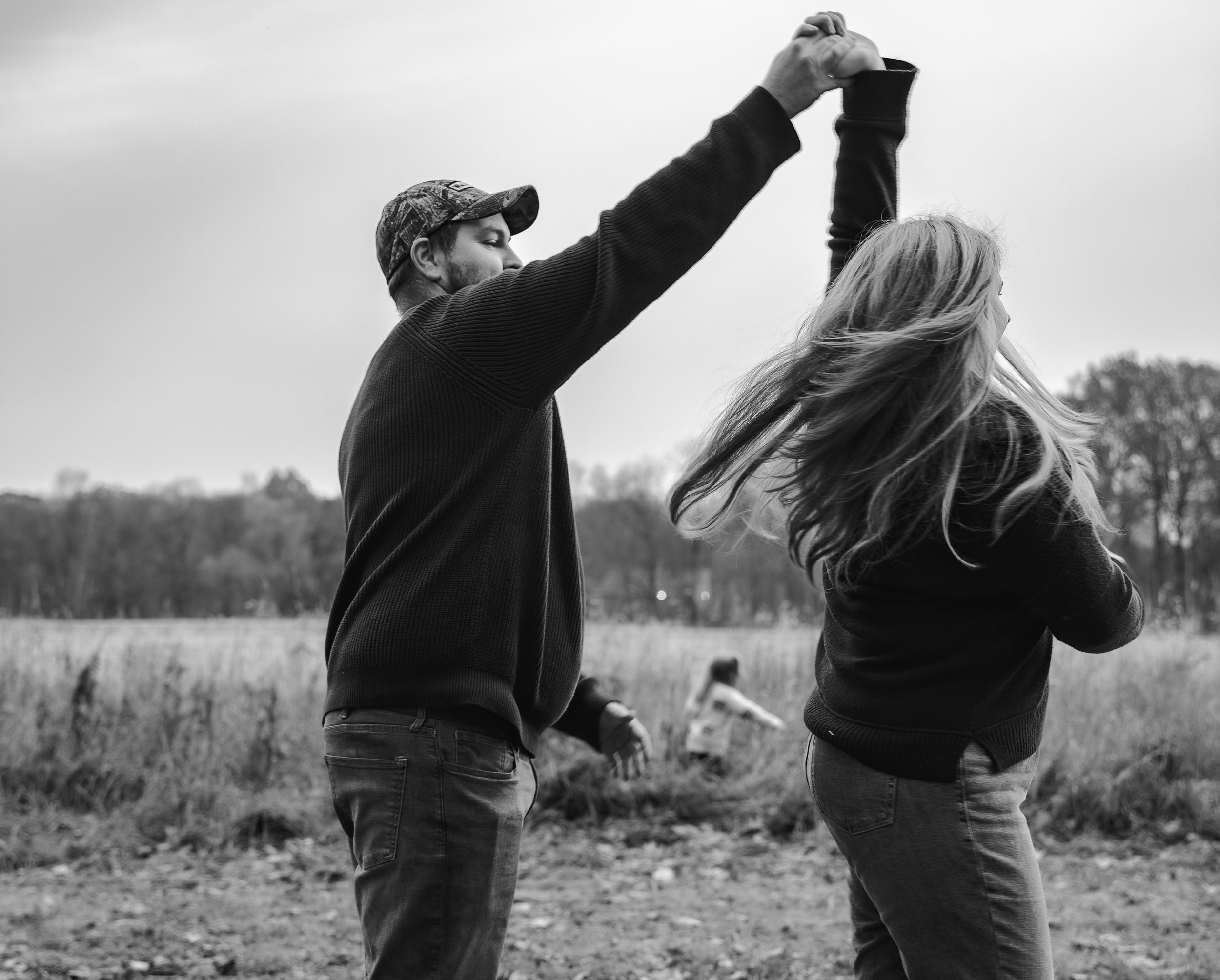 Black and white photo of a man spinning a woman in a field, with a child in the background.