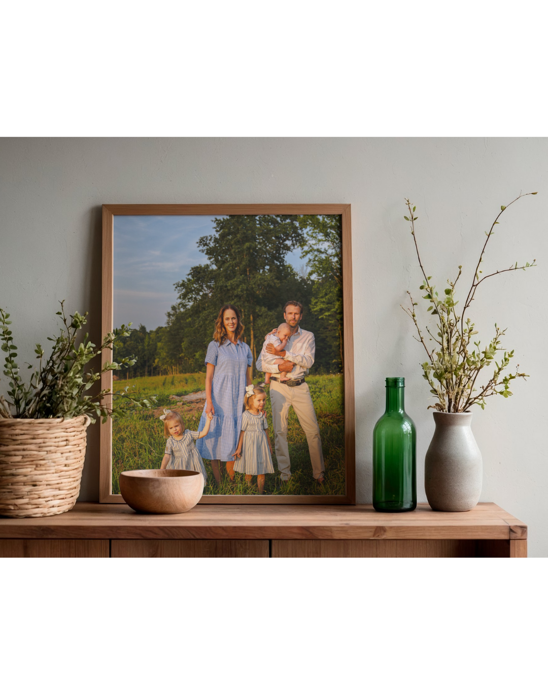A framed family portrait on a shelf, with two potted plants and a green bottle, inside a home.