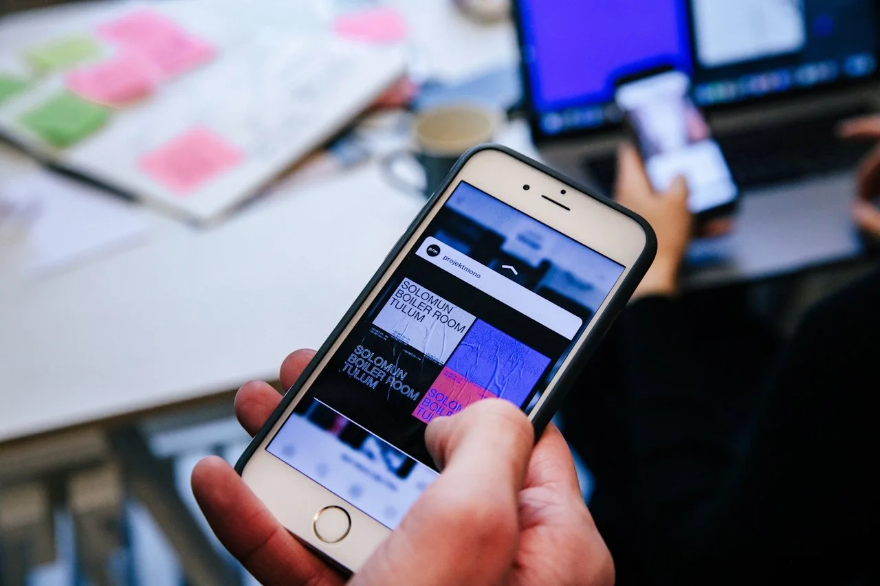 IPhone scrolling through social media posts of brand color pallets & font combos while in a brand meeting.