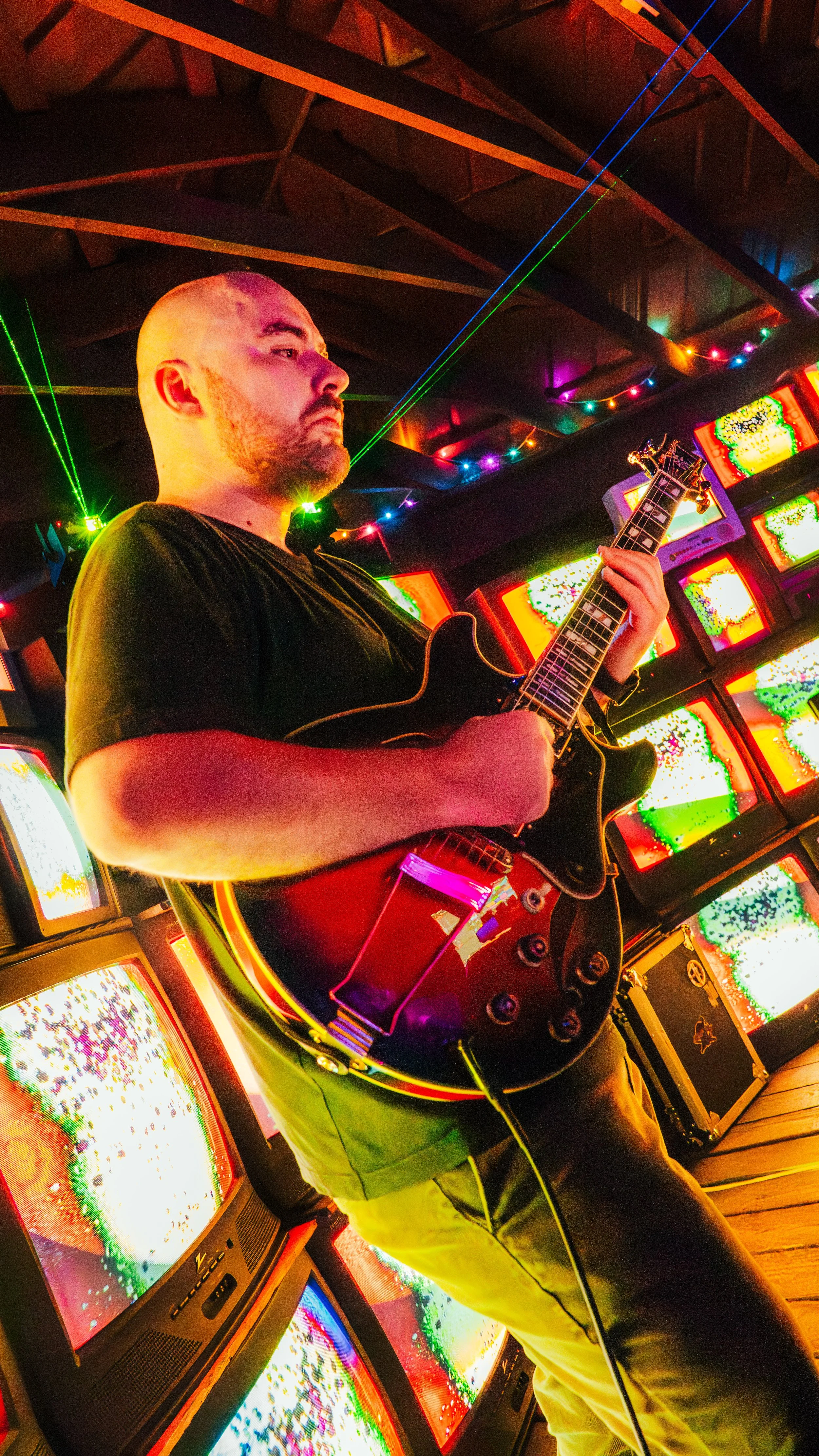A man playing an electric guitar in a room decorated with colorful, flashing arcade machines and neon lights.