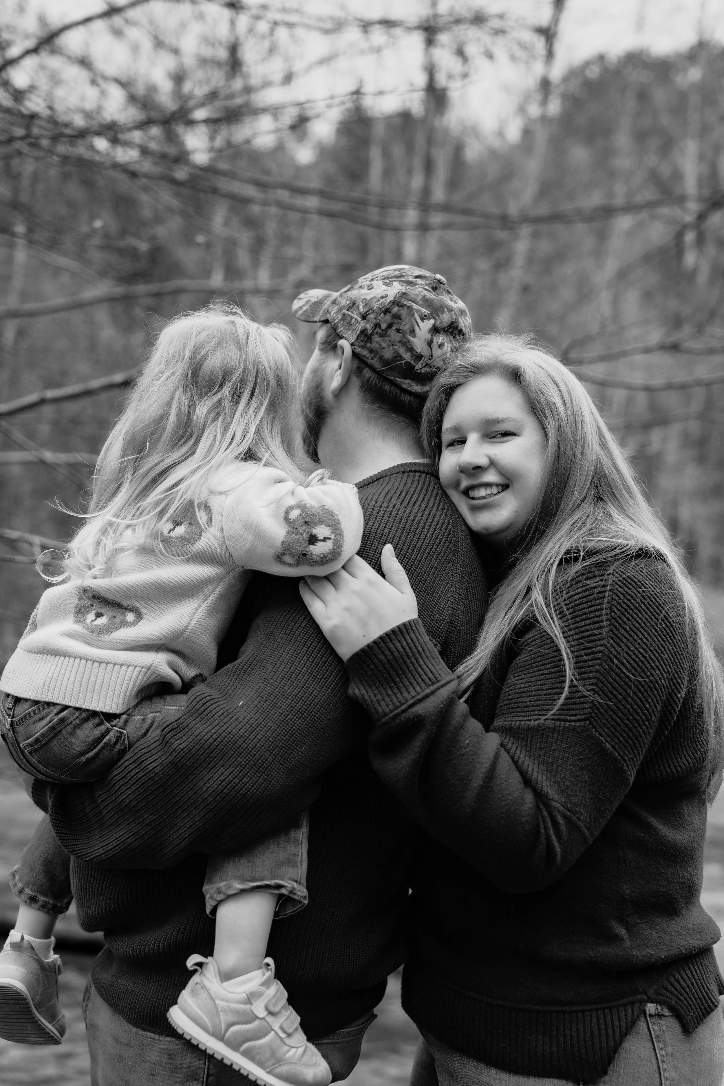 A happy family outdoors, with a man holding a young girl and a woman smiling, in black and white.