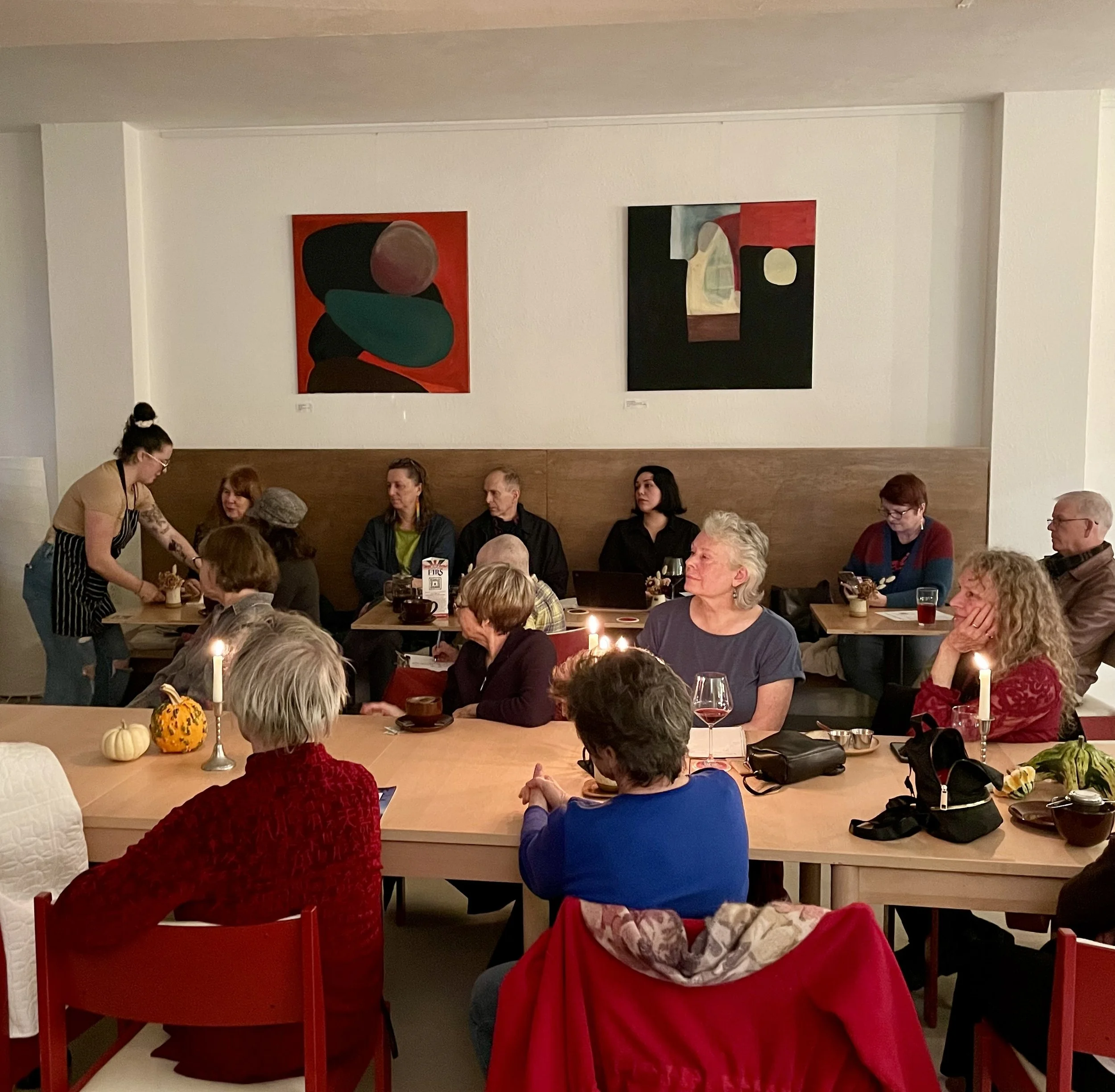 People dining at a restaurant with autumn-themed decorations on the tables, including pumpkins and candles. Artwork hung on the plain white walls.