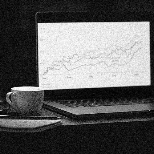 Laptop displaying a line graph, a coffee mug, and a closed notebook on a desk.
